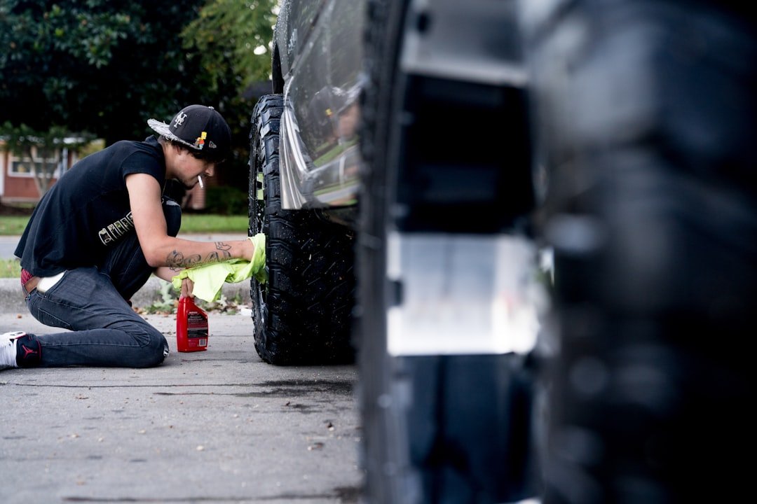 Young man covered in tattoos wipes off soap scum on his rims while smoking a cigarette.