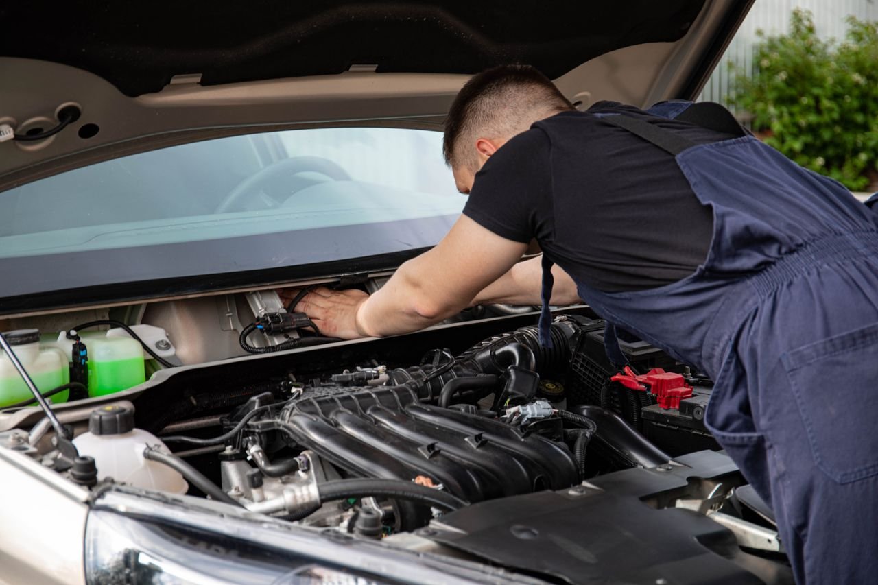Auto mechanic performs engine maintenance on a car. Focus on hands and engine components.